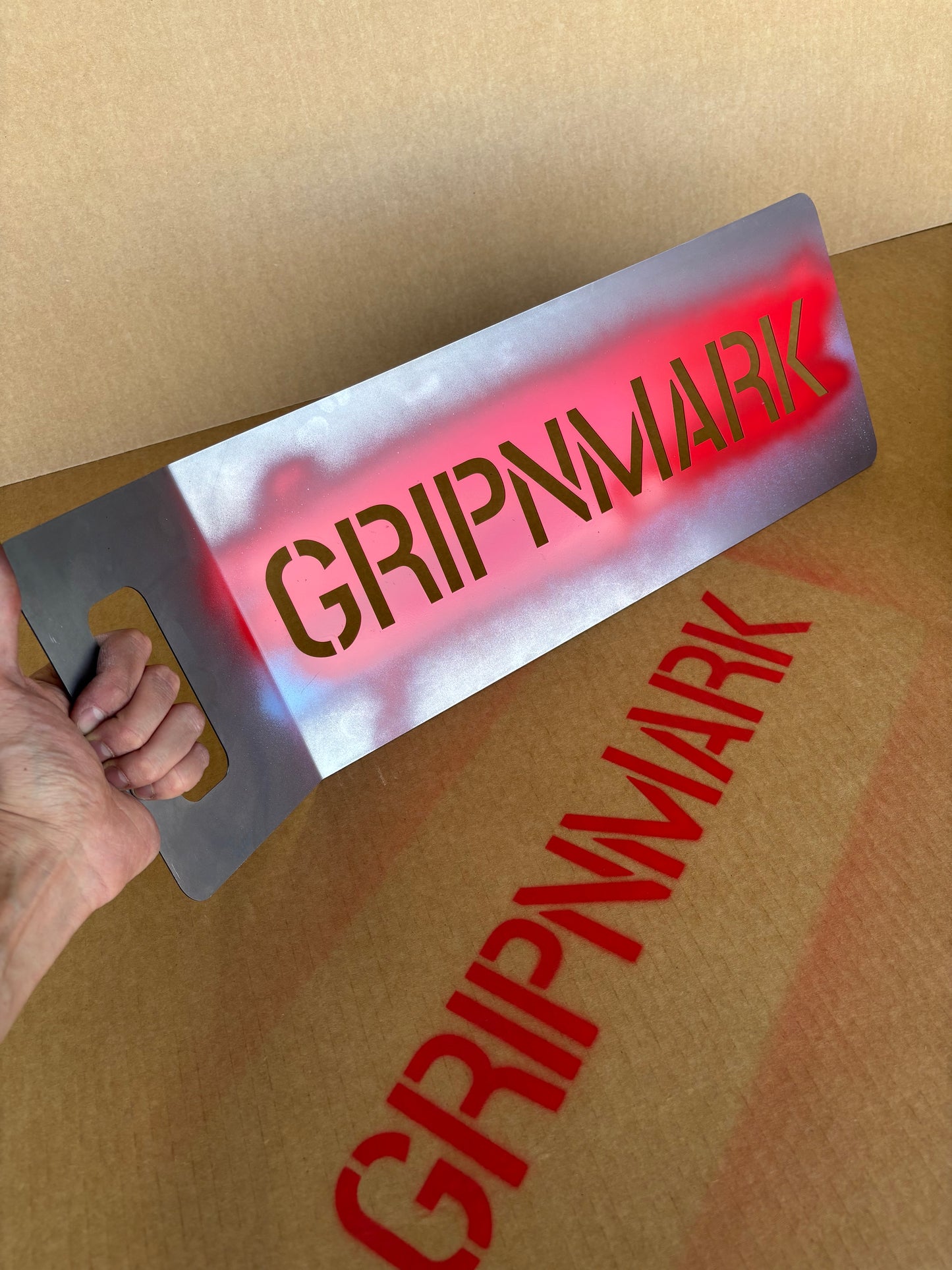 Person using a stencil with 'GRIPNMARK' branding on a cardboard surface