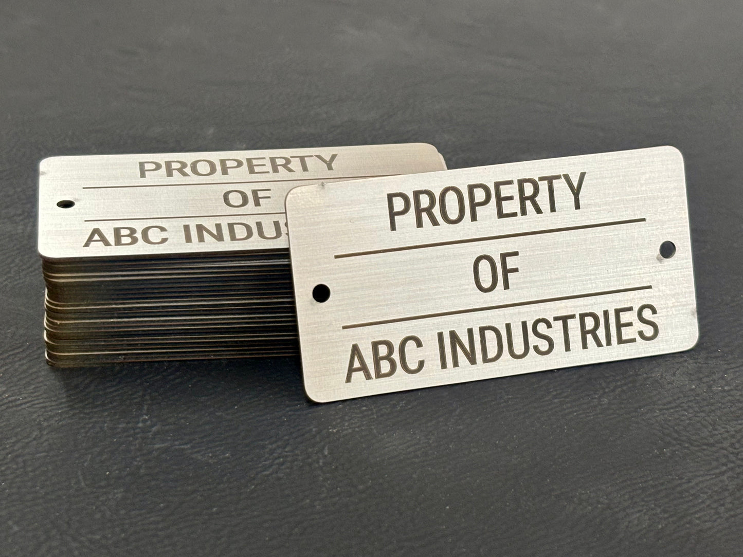 Stack of metal tags with 'Property of ABC Industries' text on a dark surface