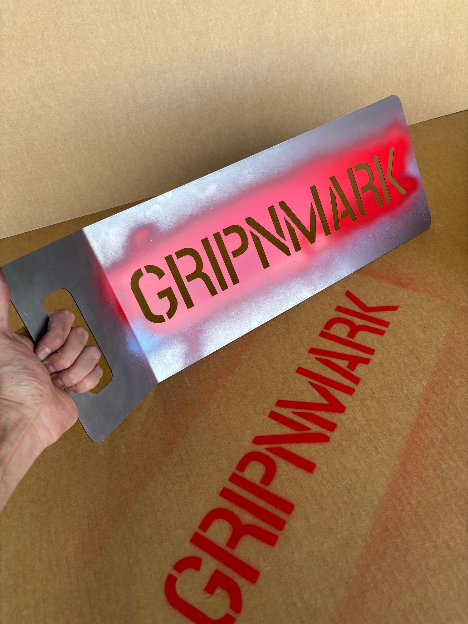 Person using a stencil with 'GRIPNMARK' branding on a cardboard surface
