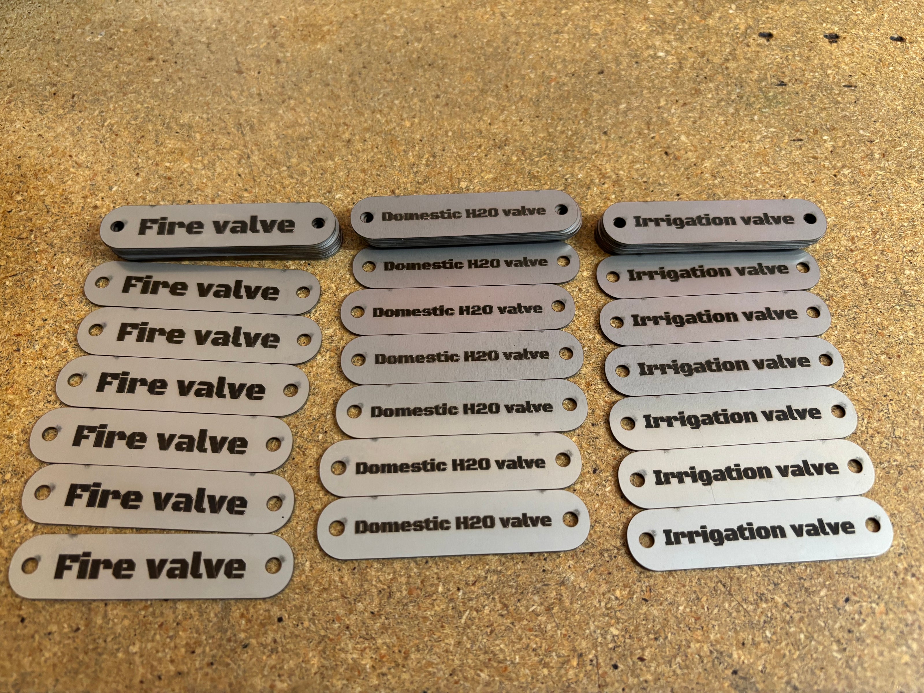 Set of valve identification tags labeled 'Fire valve', 'Domestic H2O valve', and 'Irrigation valve' on a textured surface.