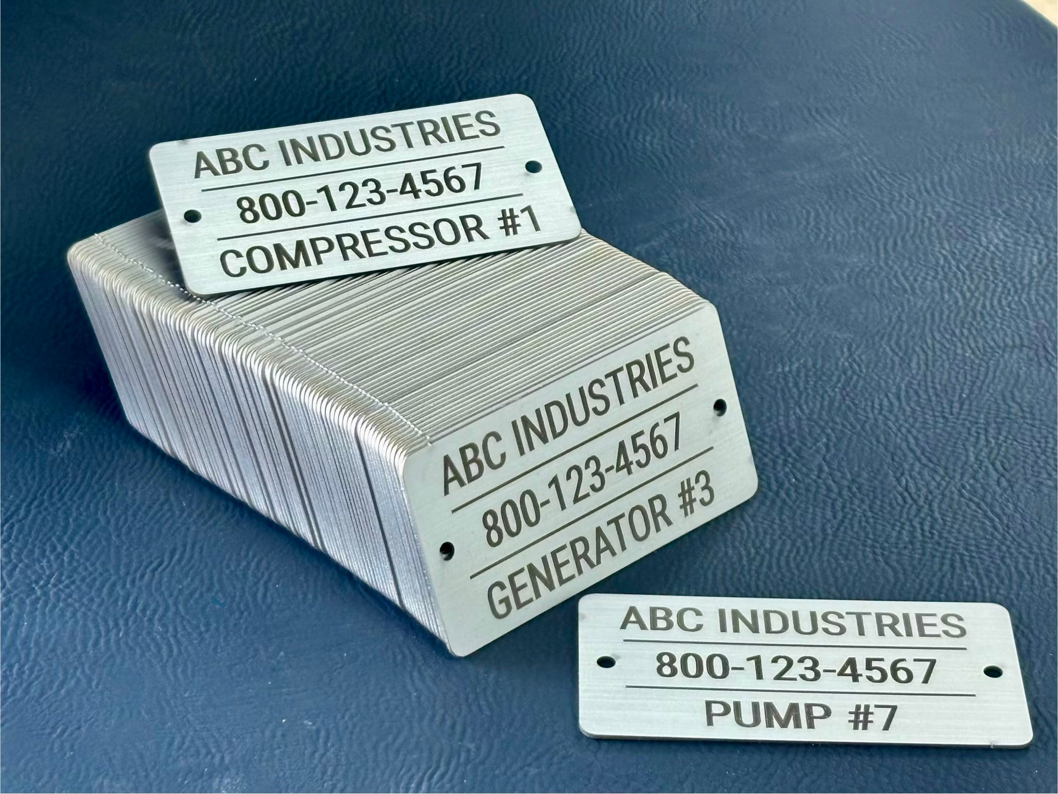 Stack of metal tags with 'ABC Industries' branding and contact information on a blue background